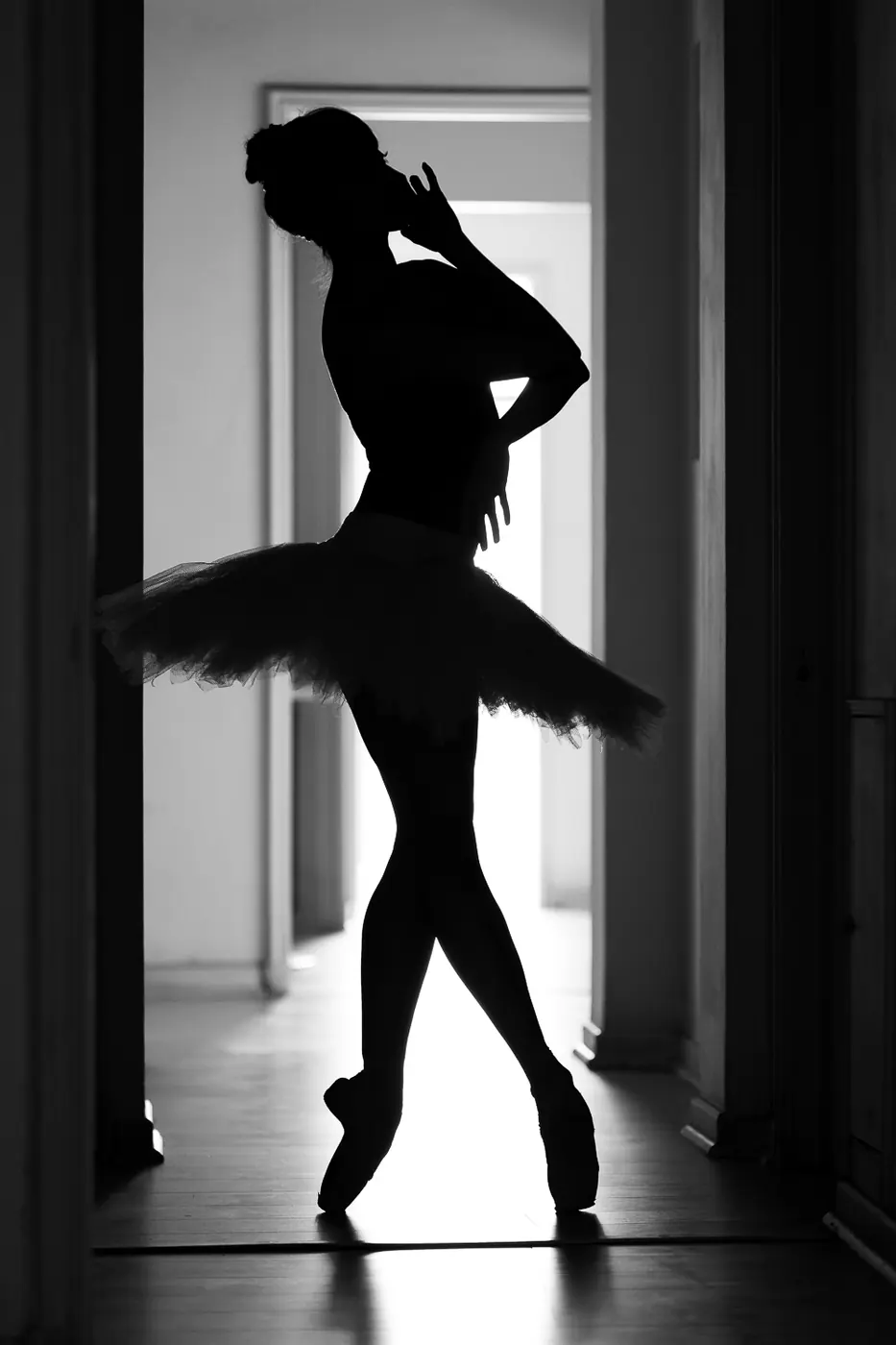 Silueta a contraluz de una bailarina con tutú sobre puntas, junto a una puerta