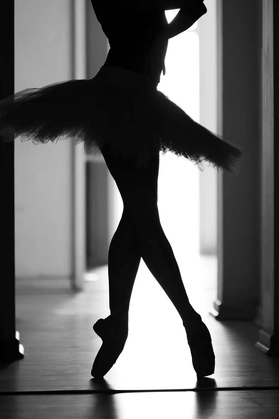 Bailarina con tutú en silueta, de pie sobre puntas frente a una ventana iluminada